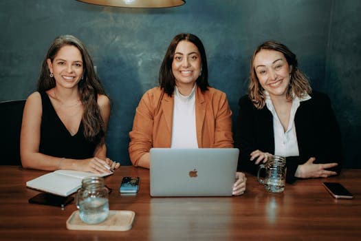Three women sitting at a table with a laptop