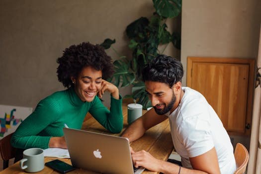 Two colleagues engaged in teamwork, brainstorming ideas on a laptop in a cozy office setting.