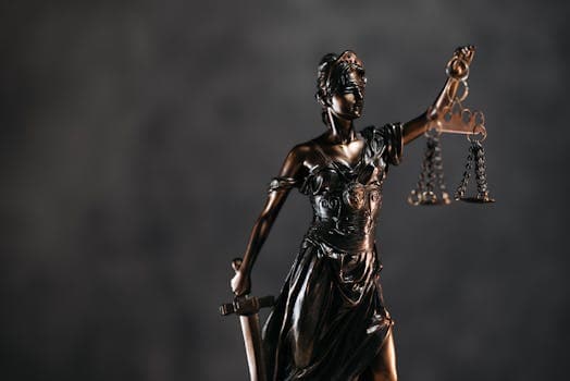 Detailed bronze Lady Justice statue with scales and sword against a dark background, symbolizing law and justice.